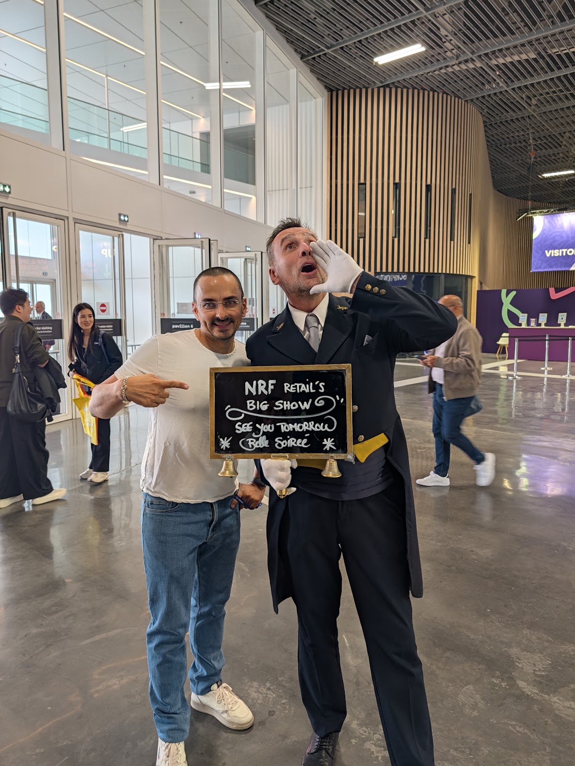Adrien pose en souriant à côté d’un homme en costume tenant une ardoise NRF Retail’s Big Show.