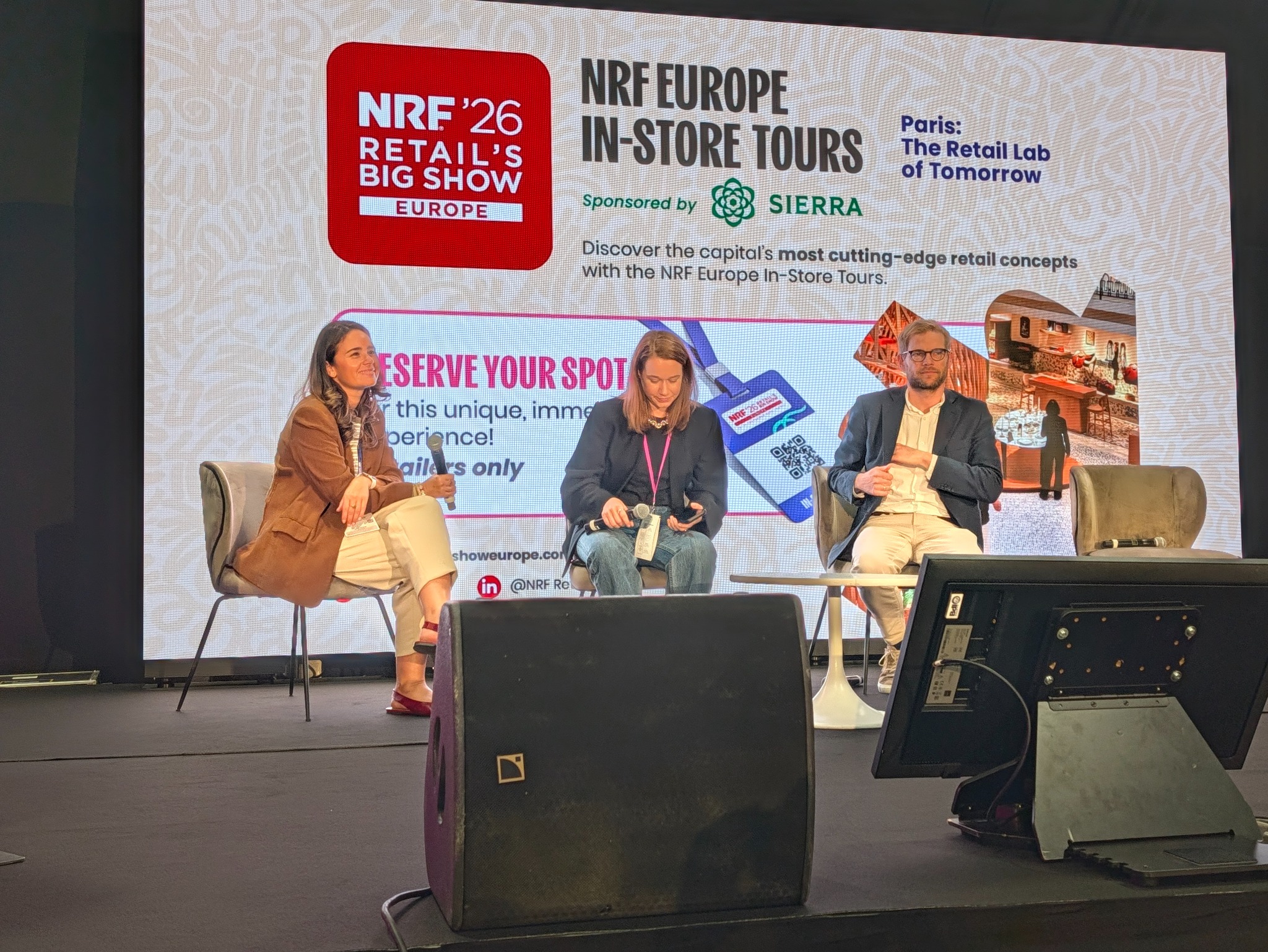 Laetitia, micro en main, sur la scène de NRF Europe avec deux autres participants.